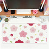 A pink floral mouse pad with various pink and green flowers and leaves placed on a wooden desk next to a computer monitor.