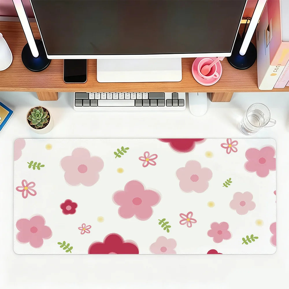 A pink floral mouse pad with various pink and green flowers and leaves placed on a wooden desk next to a computer monitor.