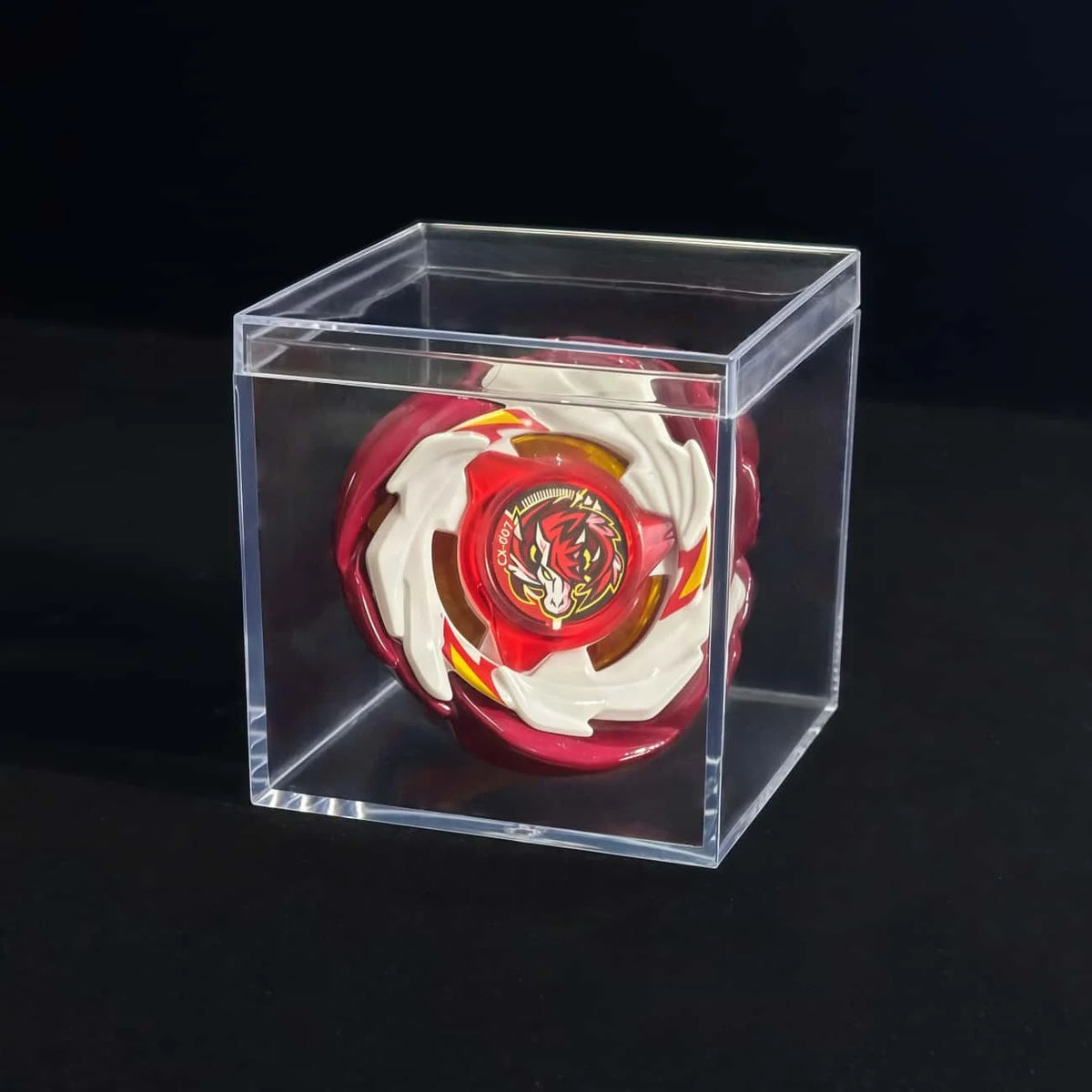 A red and white metal spinning top is displayed inside a clear plastic box.