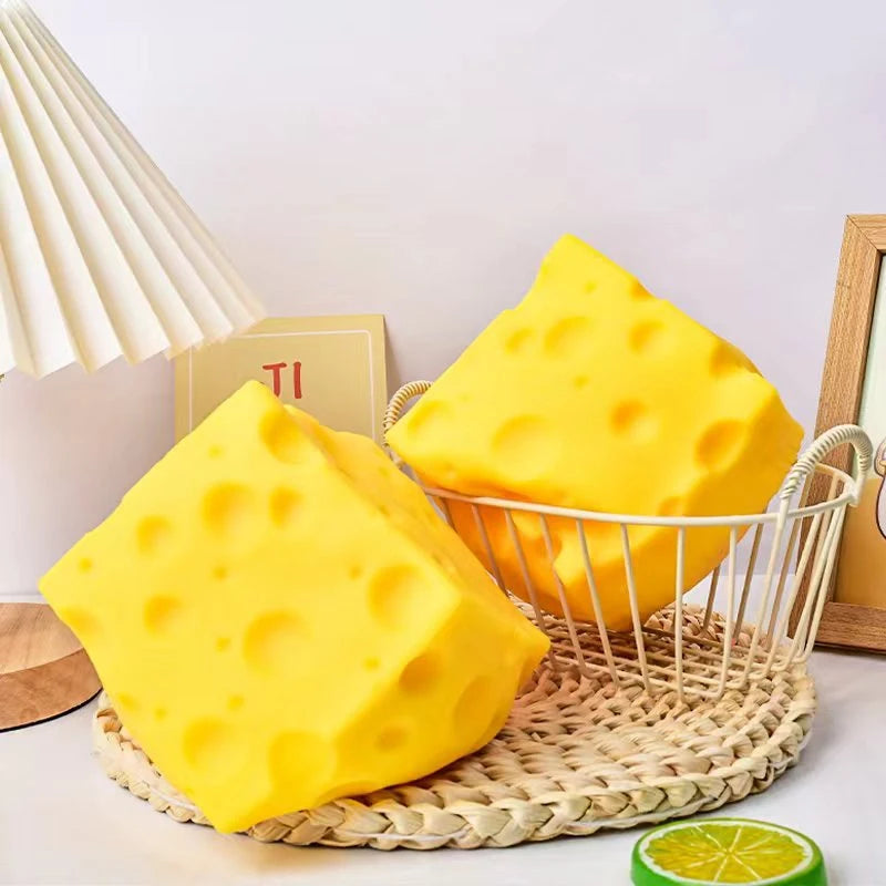 A bright yellow cheese-themed squishy stress relief toy is displayed on a woven tray next to a slice of citrus fruit.