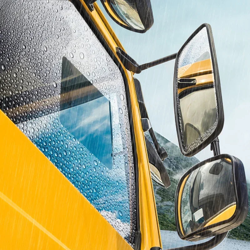 Close-up of a yellow car windshield covered in raindrops, showing a clear anti-fog and rain-repellent film on the glass.