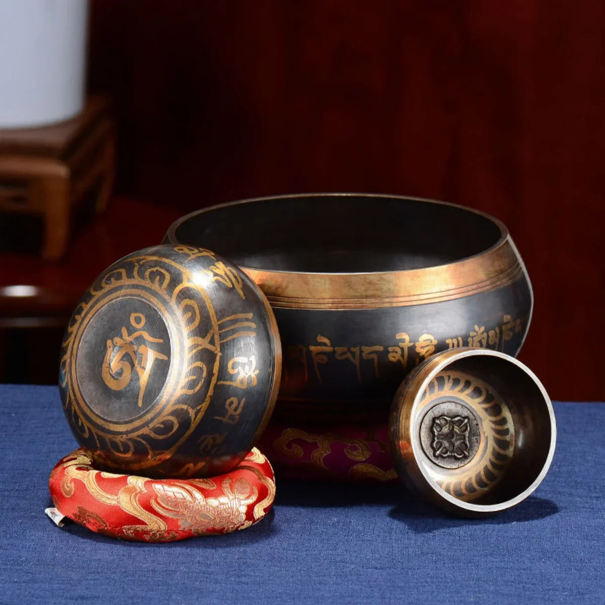 A handcrafted Tibetan singing bowl resting on a red cushion with its striker and cushion visible.