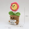 Handmade crochet doll featuring a pink flower head and green leaves growing from a brown pot with a smiling face.