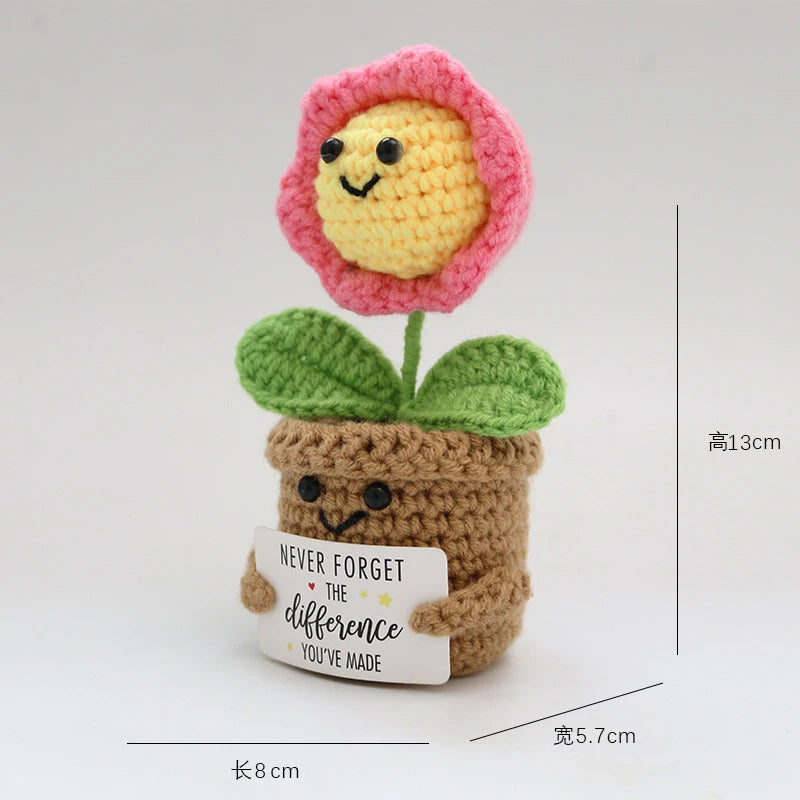 Handmade crochet doll featuring a pink flower head and green leaves growing from a brown pot with a smiling face.