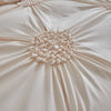 A close-up of a beige pleated duvet cover featuring a three-dimensional floral rosette detail.