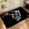 A black doormat featuring a white stylized animal head design placed on a wooden floor.