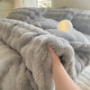 A hand is touching a fluffy gray fleece duvet cover with a rabbit design in a bright room.