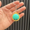 Eine Hand hält eine silberne Kette und einen runden, hellgrünen dekorativen Dumpling-Anhänger.