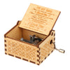 A vintage hand-cranked wooden music box with an open lid featuring engraved text and a small metal crank.