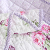 White quilted fabric featuring pink and purple floral embroidery and a lavender stitched edge.