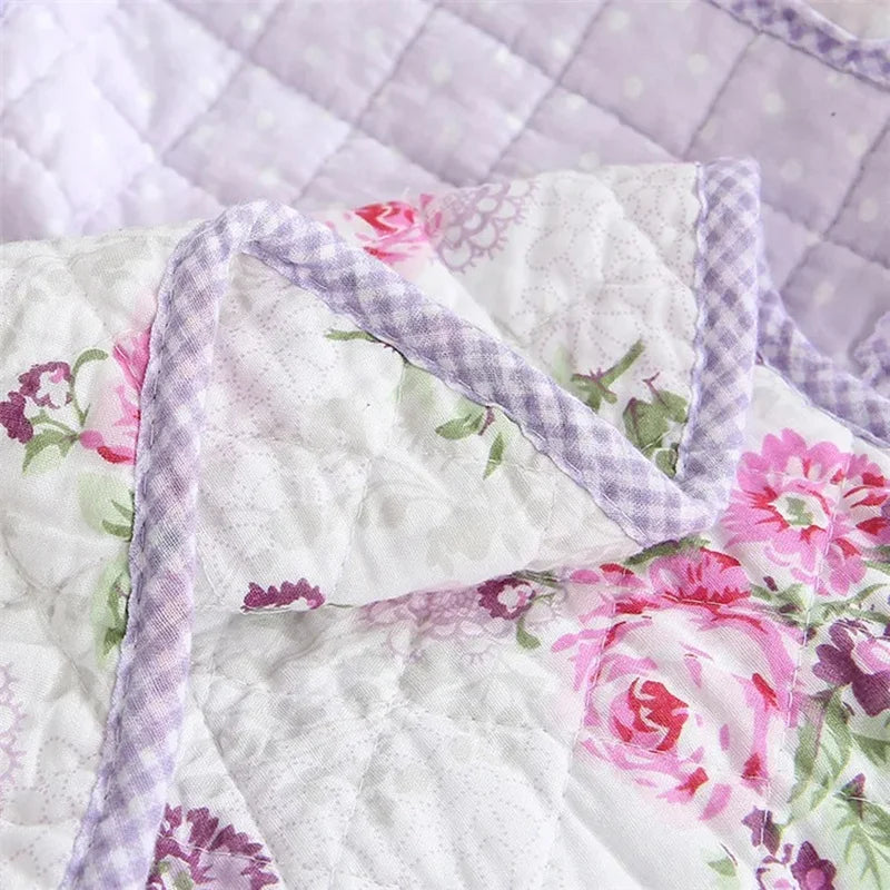 White quilted fabric featuring pink and purple floral embroidery and a lavender stitched edge.
