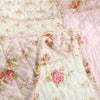 Close-up of a pink and white floral patchwork quilt featuring quilted fabric and embroidery details.