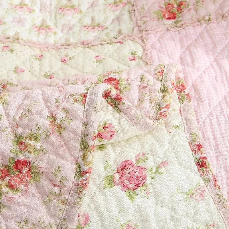 Close-up of a pink and white floral patchwork quilt featuring quilted fabric and embroidery details.