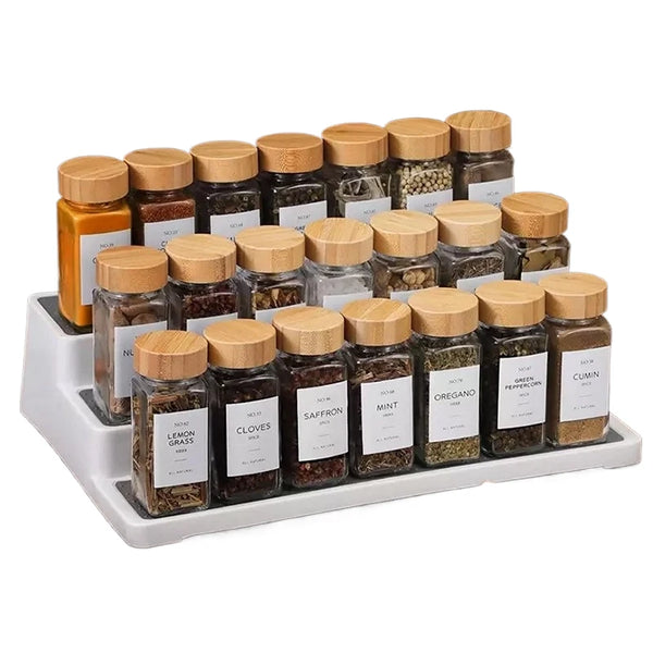 Collection de pots à épices en verre transparent avec couvercles en bambou, remplis d'épices moulues, dans un support blanc.