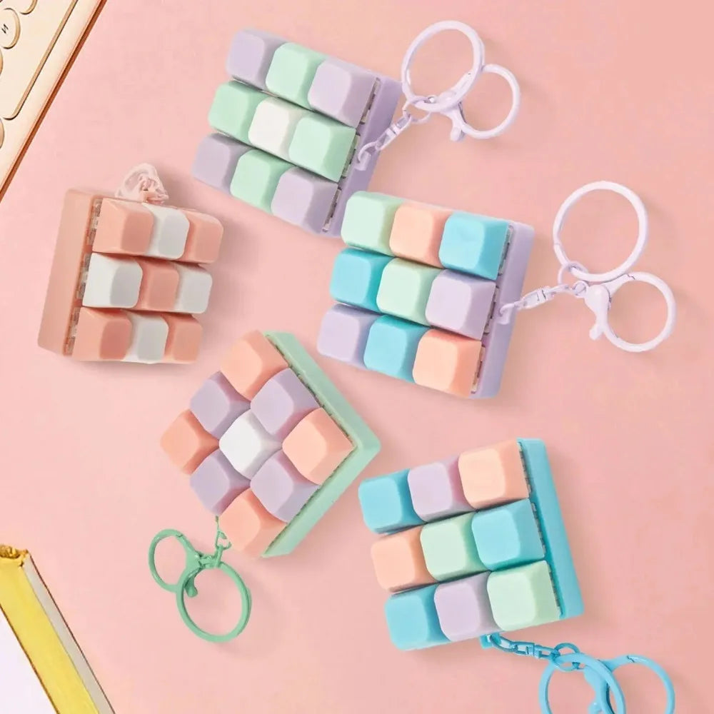 A collection of pastel colored mini keyboard fidget keychains arranged on a pink background.
