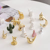 A collection of handcrafted ceramic elephant and rabbit jewelry holders and desk ornaments in gold and white.