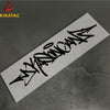 A black wildstyle graffiti decal on a white sticker placed on a dark gray surface.