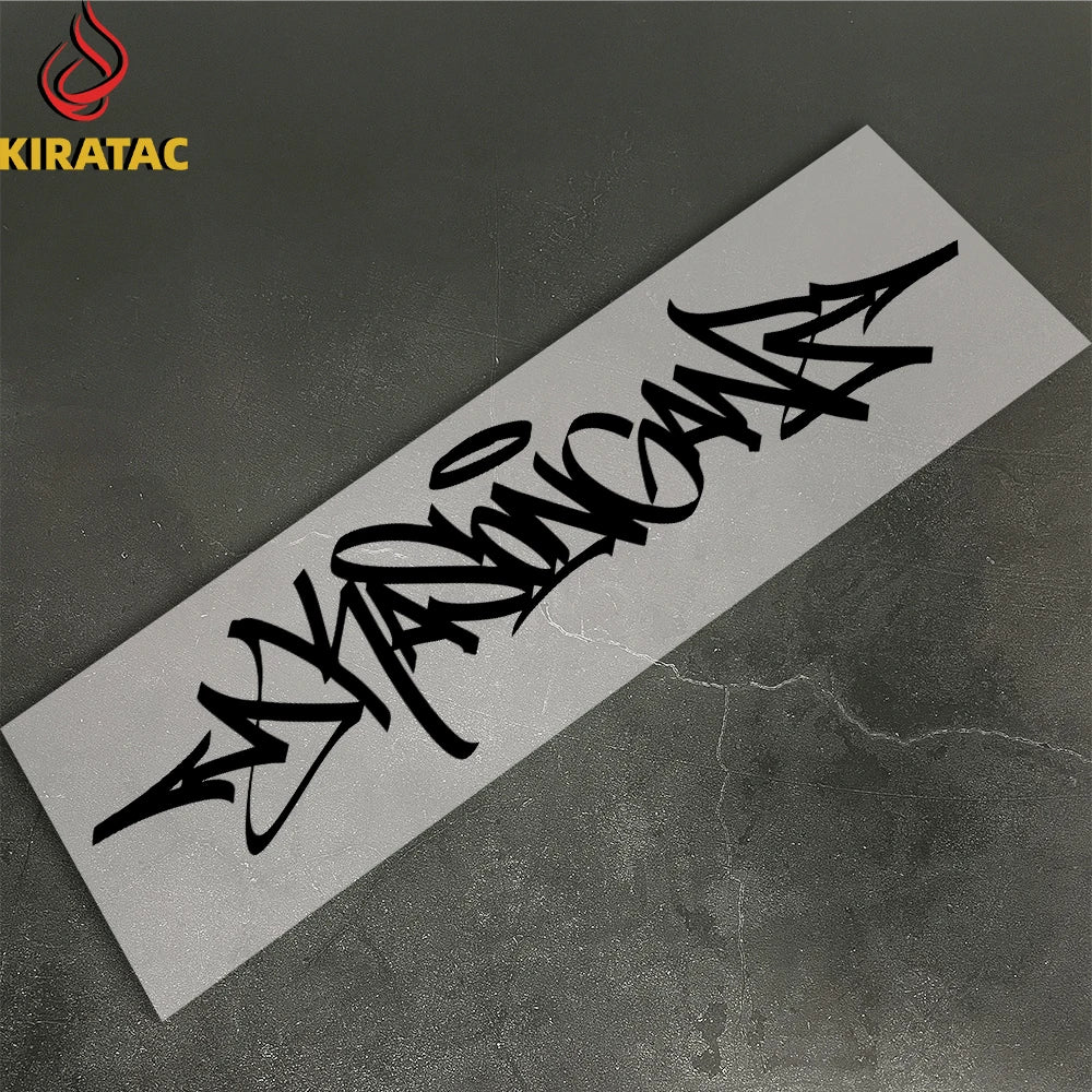 A black wildstyle graffiti decal on a white sticker placed on a dark gray surface.