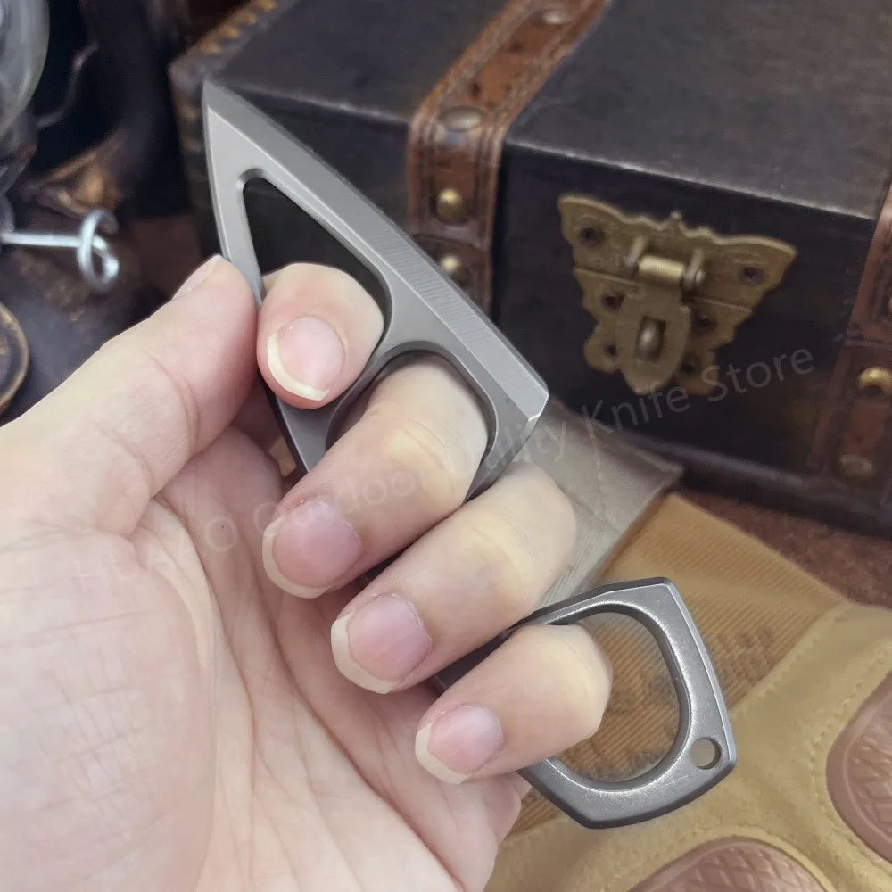 A hand holds a compact stainless steel neck knife with its sheath resting on a brown leather box.