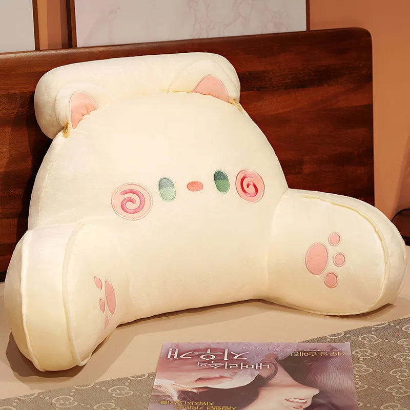 A cream-colored plush cushion shaped like a cat's head with pink accents, used as a backrest for furniture.