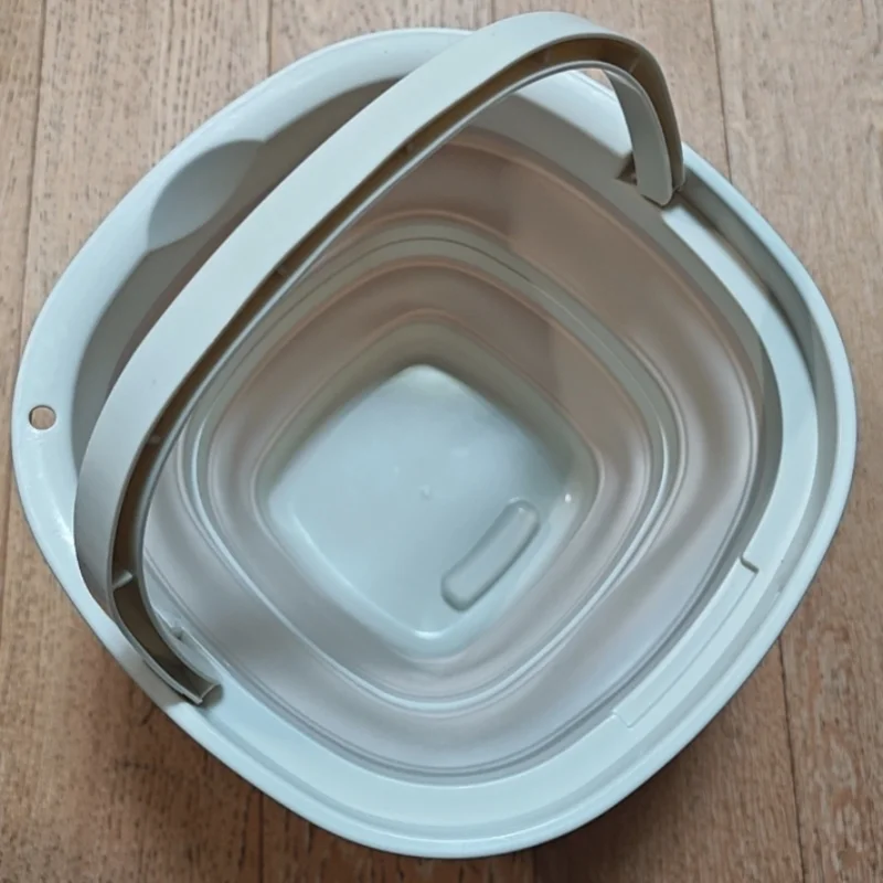 A white collapsible portable bucket with a handle is shown on a wooden surface.