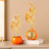 A golden, leaf-shaped ceramic sculpture rests on an orange sphere, displayed on a white book.