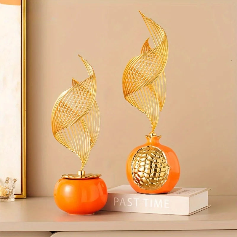 A golden, leaf-shaped ceramic sculpture rests on an orange sphere, displayed on a white book.