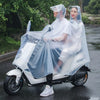 Two women wearing transparent waterproof motorcycle rain ponchos ride a white scooter on a wet road.