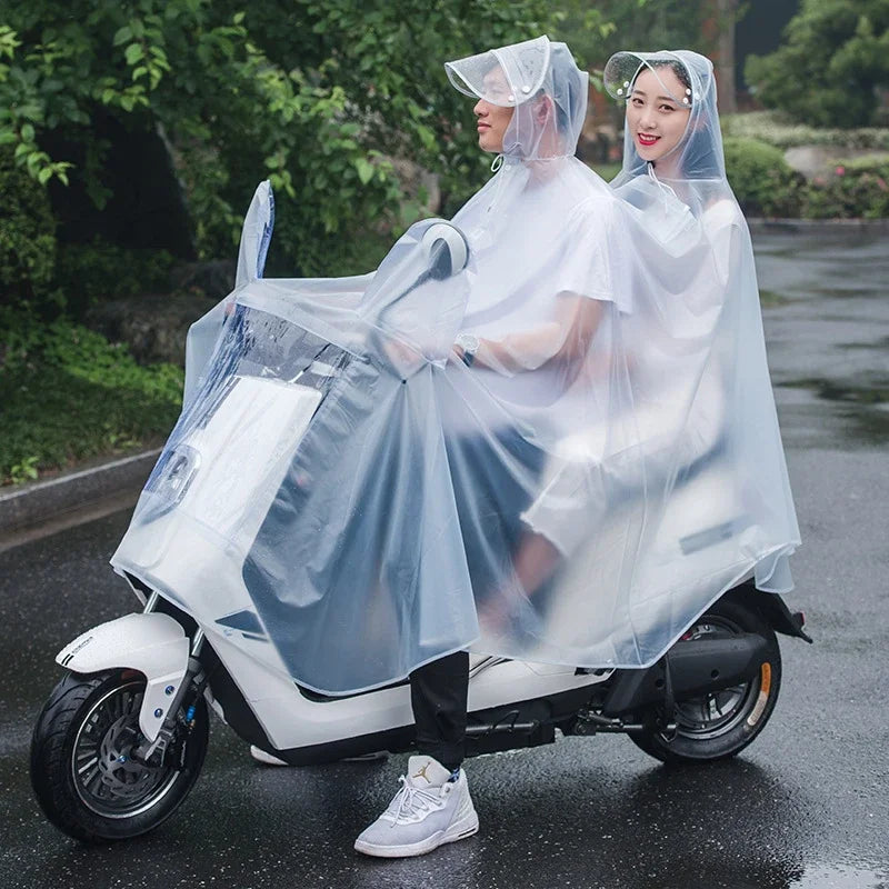 Two women wearing transparent waterproof motorcycle rain ponchos ride a white scooter on a wet road.