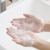 A person's hands are covered in white soap bubbles while washing them under a faucet.