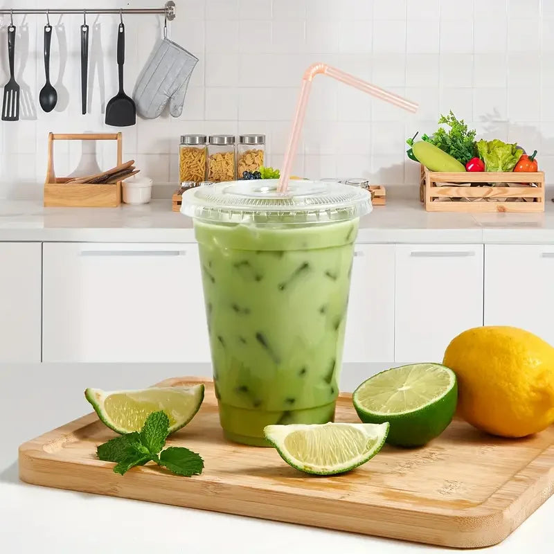 A tall green beverage in a clear plastic cup sits on a wooden board with lime slices and a lemon.