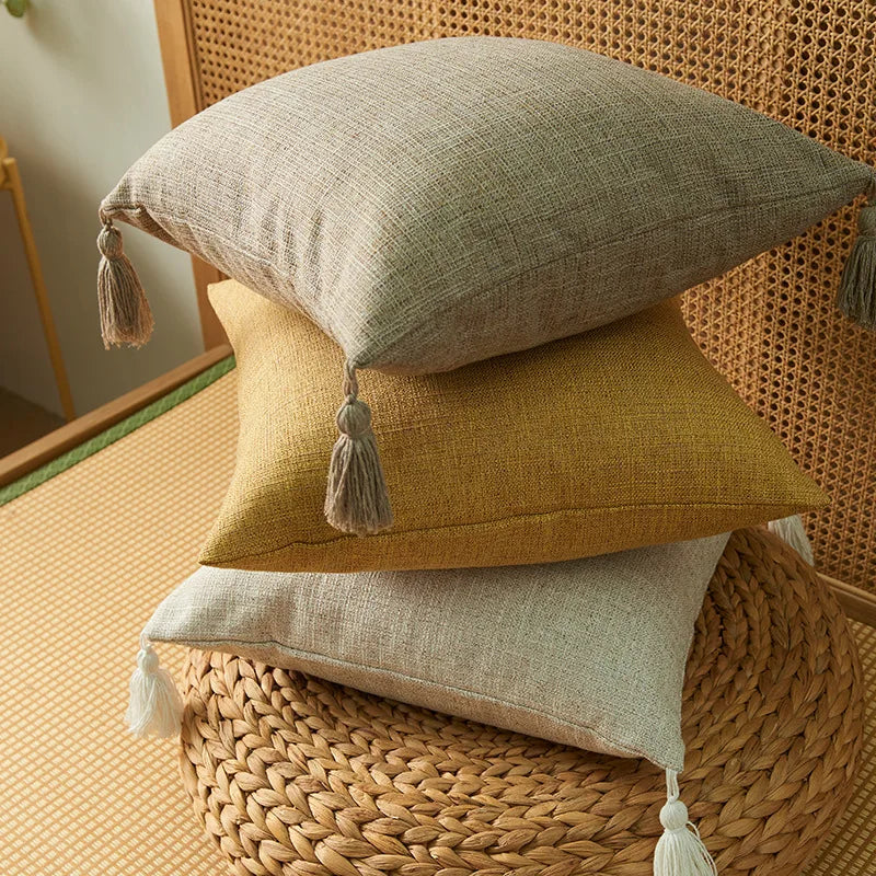 Three linen throw pillows in beige, mustard yellow, and natural linen resting on a woven basket.