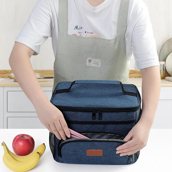 A person holds a dark blue insulated leakproof tote bag containing an apple and a banana.