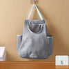 A gray mesh garbage bag holder is mounted on a wall with hooks, designed to keep bags accessible.