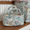A quilted fabric storage basket in light blue and cream floral pattern sits on a wooden shelf.