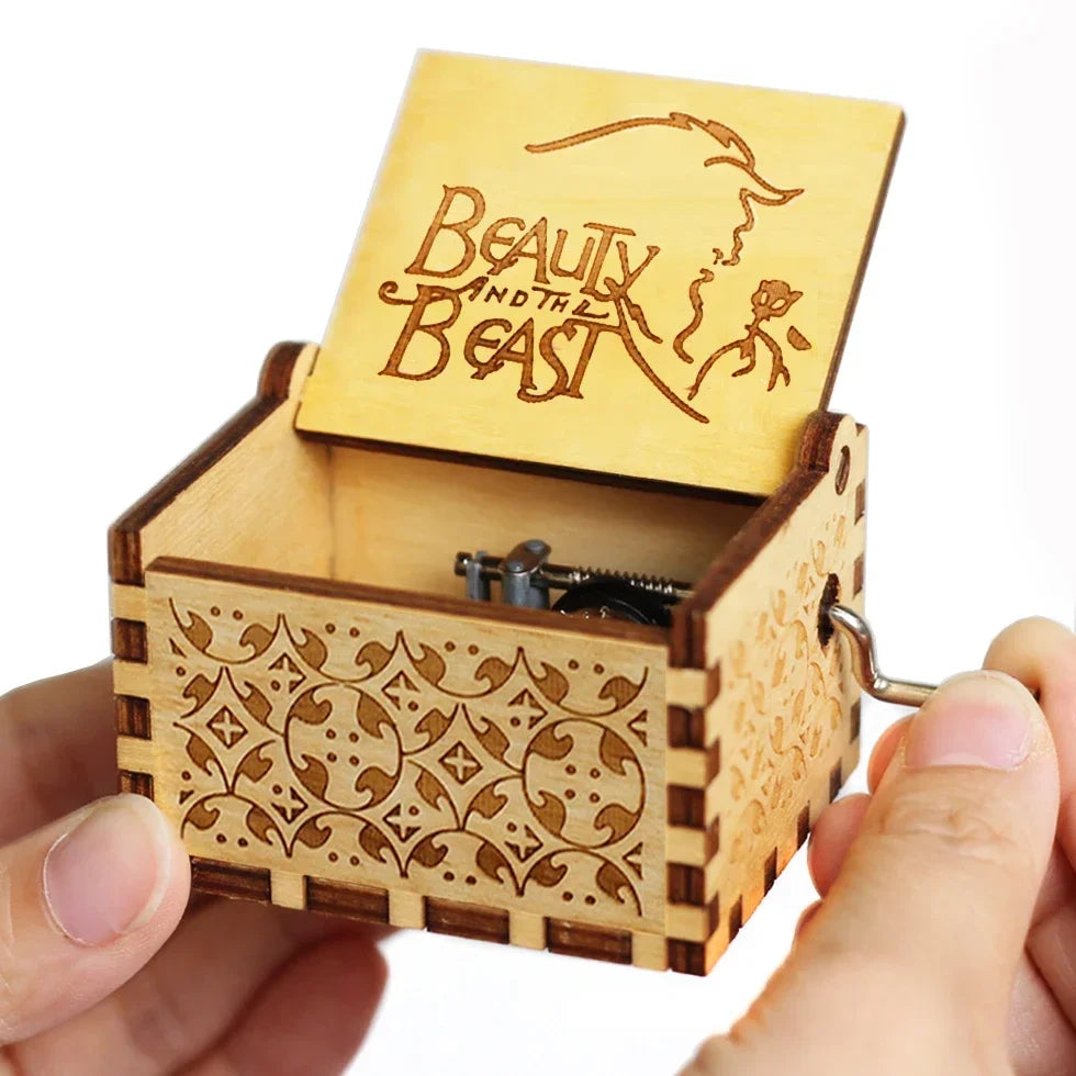 A vintage hand-crank wooden music box with a lid featuring the text Beauty and the Beast, made of light wood.