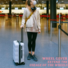 A person is standing in an airport terminal with a rolling suitcase on the floor.