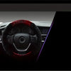 A close-up view of a steering wheel covered in a dark material with red accents, likely a plush cover.