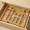 A wooden drawer organizer holding various silver and stainless steel cutlery in individual slots.