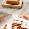 A collection of natural bamboo soap dishes and a wooden brush are displayed on a light gray towel.