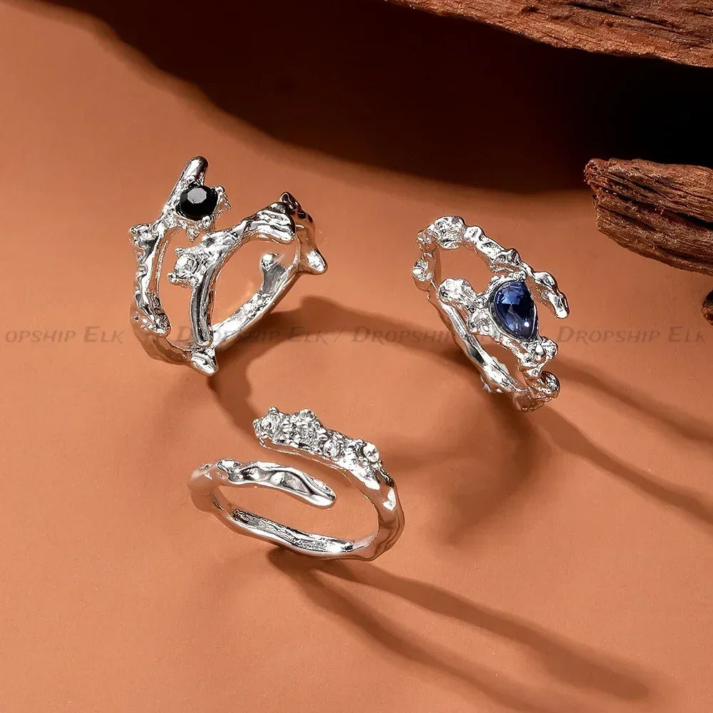 Silver irregular heart ring with black and blue gemstones displayed on a brown background.