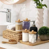A set of clear apothecary jars with wooden lids and a pump dispenser for bathroom organization on a white countertop.