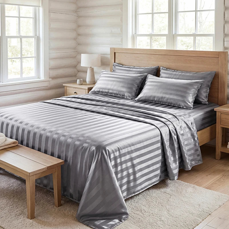 A gray and white striped satin bedding set displayed on a wooden bed with natural light.