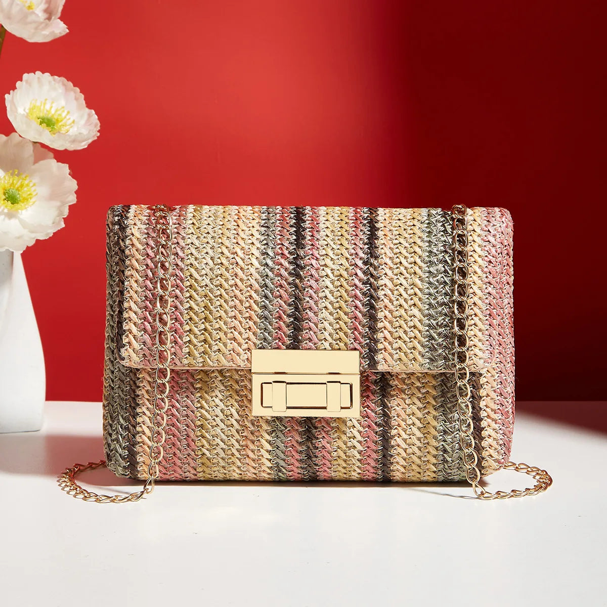 Sac bandoulière bohème tissé à rayures multicolores avec une chaîne dorée, posé sur une surface blanche.