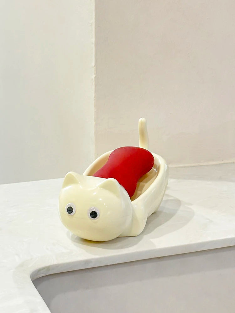 A white cat-shaped soap box with a red drainage tray sits on a white surface.
