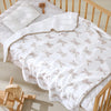 White cotton gauze baby swaddle blanket with a bear print, draped on a wooden crib.
