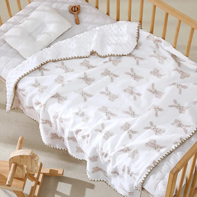 White cotton gauze baby swaddle blanket with a bear print, draped on a wooden crib.