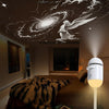 A white star projector night light illuminates a ceiling mural of a winged angel and galaxy in a bedroom.
