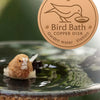 A round copper disk for a bird bath is shown with a small bird resting in the water.