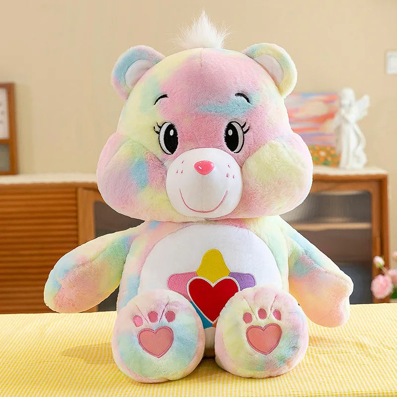 Peluche de Care Bears arcoíris rosa y multicolor con cara sonriente y detalles de corazón.